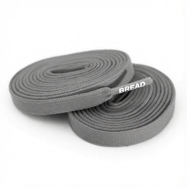 Two coiled gray fabric shoelaces with BREAD printed on the plastic tip.