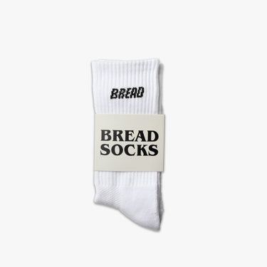 White crew socks with "BREAD" printed in black on the cuff, packaged with a label reading "BREAD SOCKS.