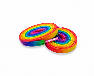 Two rolls of rainbow-colored elastic shoelaces with a pink center band labeled 'BREAD' on a plain white background.