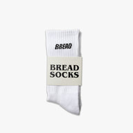White crew socks with "BREAD" printed in black on the cuff, packaged with a label reading "BREAD SOCKS.