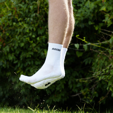 White crew socks with "BREAD" text, worn by a person jumping outdoors against a green background.